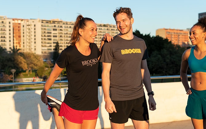 A runner stretches and laughs with two fellow runners.