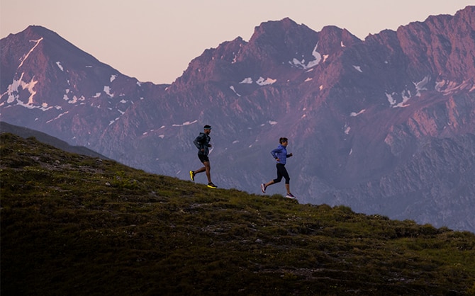 Dos corredores bajando una colina con picos a lo lejos