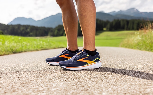 Close-up of someone's feet wearing the Ghost 15 on a sidewalk or trail and mountains in the background