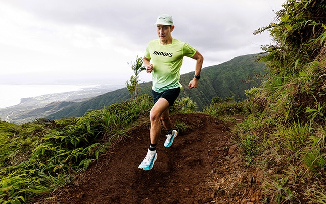 Trail runner on a mountain path overlooking Maui's coastline.