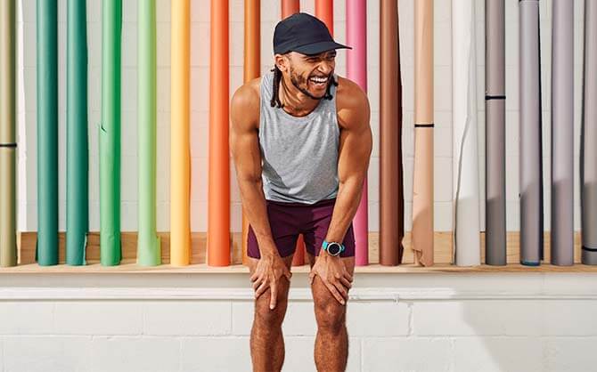 Ein Läufer, der sich lächelnd nach vorne lehnt, vor einem bunt dekorierten Hintergrund