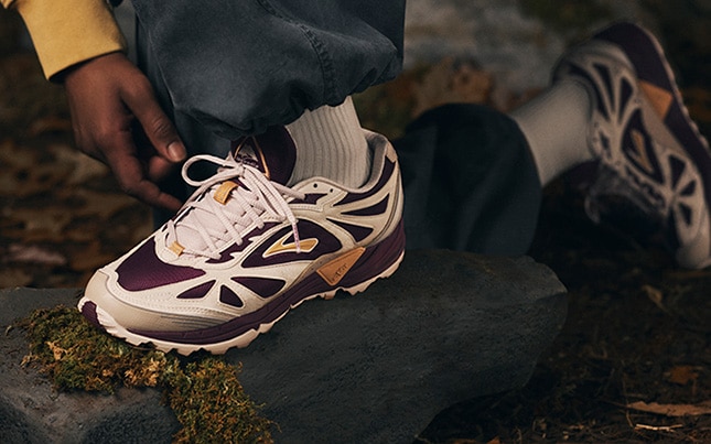 Close up of someone wearing the Brooks Cascadia 1 shoes while kneeling on leaves and rocks