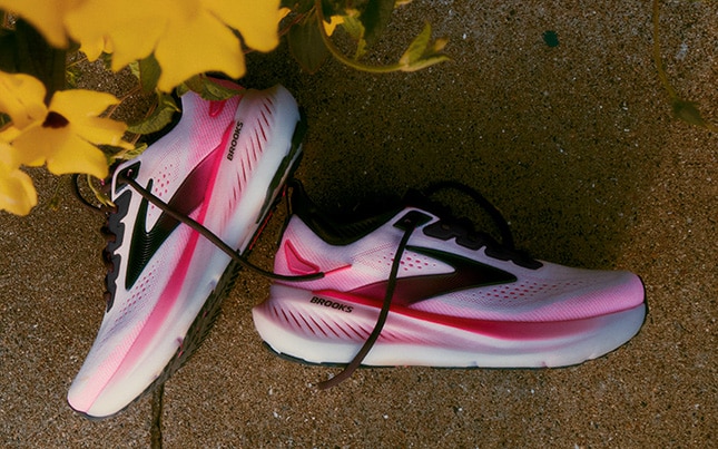 une paire rose de Brooks Glycerin 23 posée sur du béton, avec des fleurs jaunes dans le coin