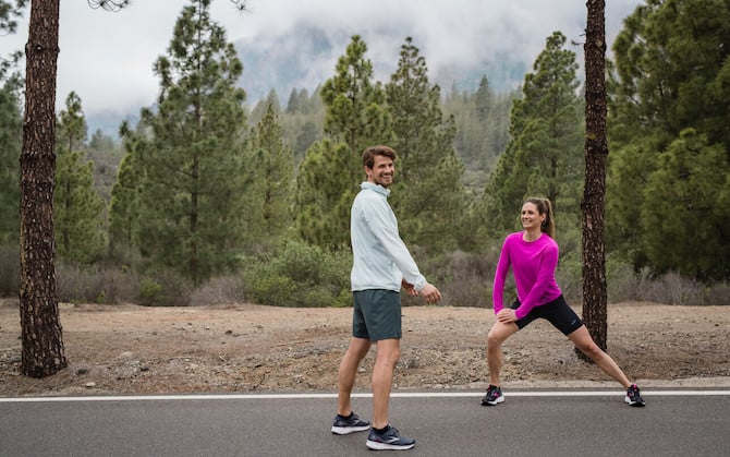 Two runners perform dynamic exercises to warm up before running.