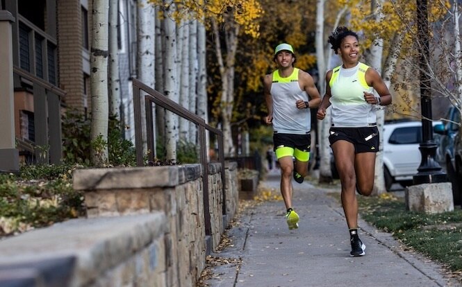 Zwei Läufer joggen auf einer Straße und tragen reflektierende Kleidung.