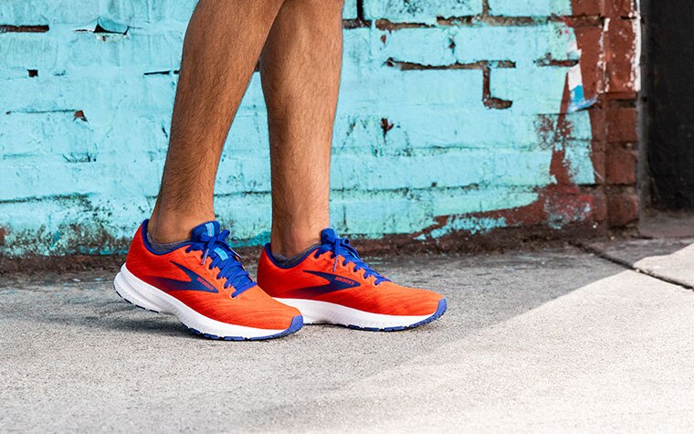 Runner standing in front of a blue wall wearing the Launch in a bright red colorway.