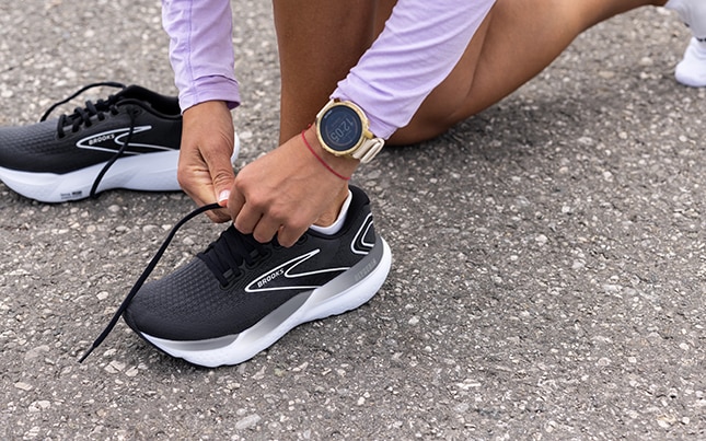 Runneuse qui lace sa chaussure de running Brooks sur du bitume