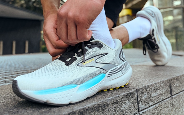 Runner laçant ses chaussures de running Brooks dans un environnement urbain