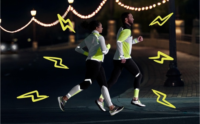  Dos corredores cruzan una carretera por la noche, todos llevan la equipación Run Visible.