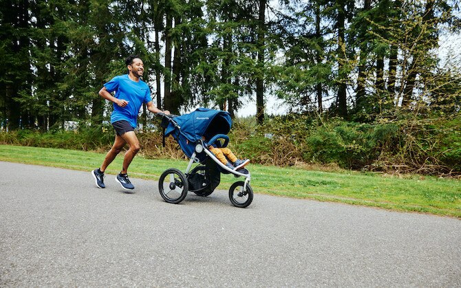A parent runs with their baby in a stroller.