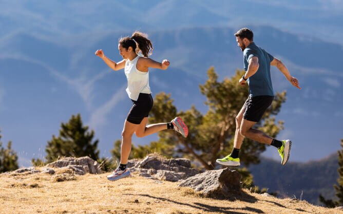 Two people trail running on a sunny hillside