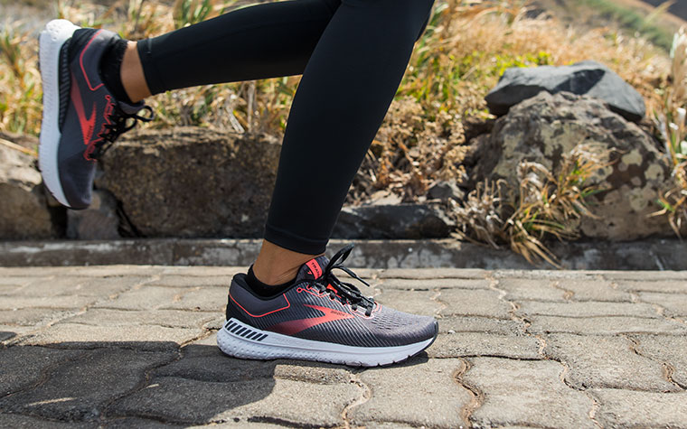 A runner strides along a paved road wearing a pair of grey and red Transcend shoes.