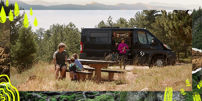 A man sitting at a picnic table with two kids while a woman standing next to a van