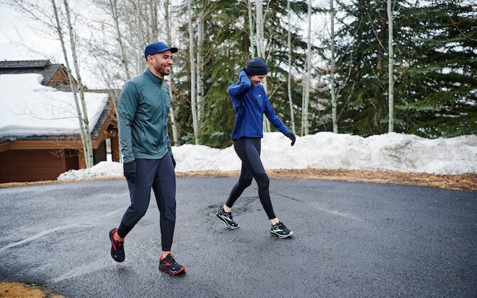 Zwei Läufer*innen tragen mehrere Schichten Bekleidung, um sich auf einen Winterlauf vorzubereiten.