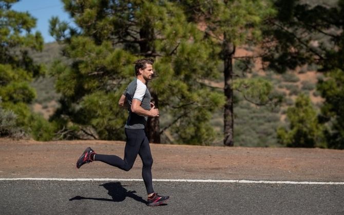 Vue latérale d’un runner sur une route bordée d’arbres.