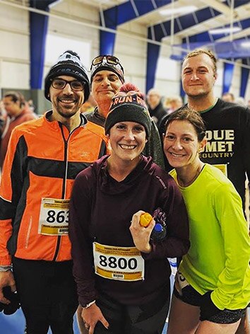 A group of five runners, all with bib numbers, pose together after a race.