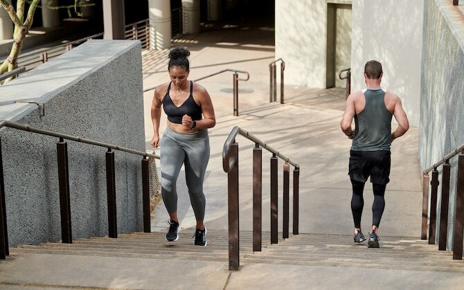 Two runners go up and down a set of stairs, respectively, in an urban environment.