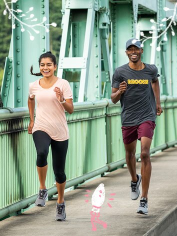 A man and a woman wearing shorts and light, warm weather shirts run happy over a bridge. 