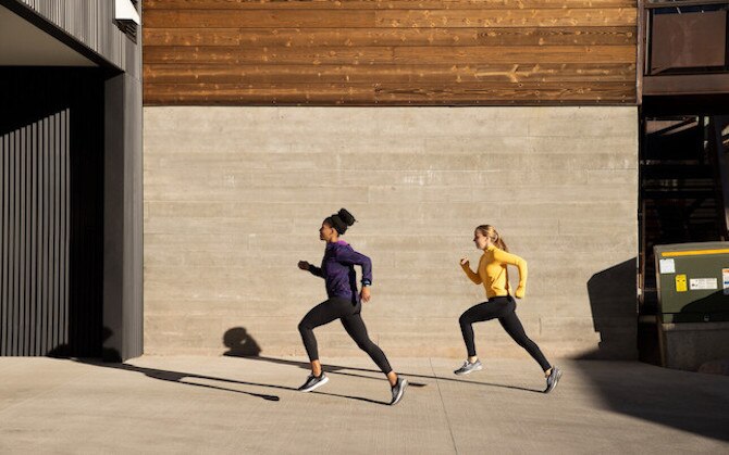 Two runners sprint on a sidewalk during high-intensity interval training.