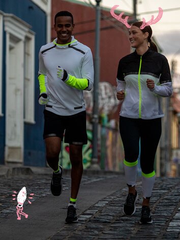 Un homme et une femme portant des vêtements réfléchissants Brooks Run Visible courent le soir.
