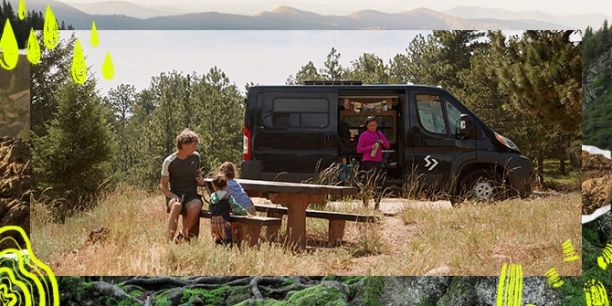 A man sitting at a picnic table with two kids while a woman standing next to a van