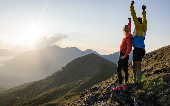Two runners in mountains with sun coming out of the clouds