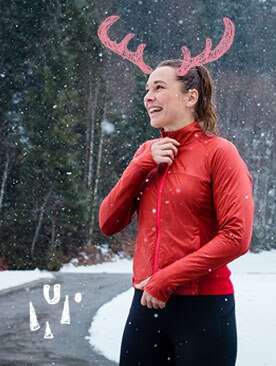 Une femme souriante en train d’enfiler une veste rouge alors qu’elle se prépare pour une course dans la neige.