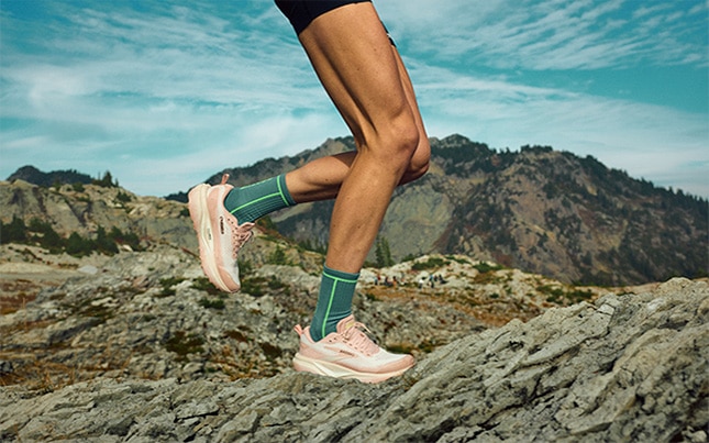 Someone running in the Cascadia 20 trail running shoes on a rocky trail with mountains in the background