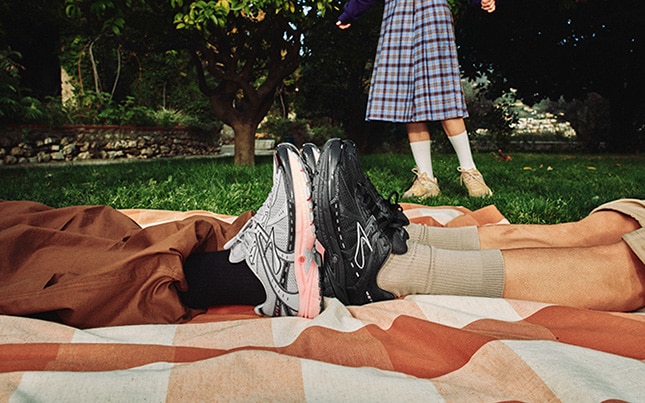 Close up of two people wearing the Brooks Adrenaline GTS 10 shoes with their feet touching while on a blanket in the grass