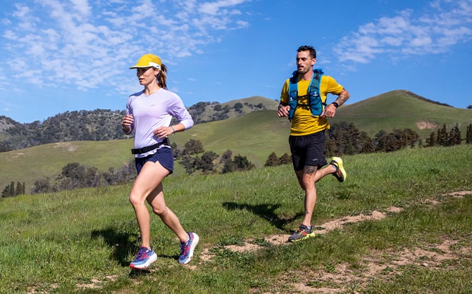 Deux runners sur un sentier avec une vue dégagée sur des collines verdoyantes