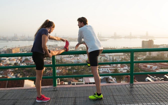 Two runners use a fence to help stretch after running.