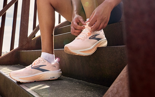 Close-up of someone’s feet wearing the Ghost 18 and tying one of the shoes while sitting on the concrete stairs
