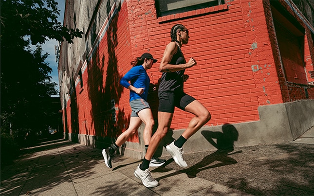 two people running in the Brooks Adrenaline GTS 25 around a street corner with a red brick building