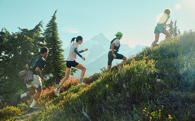 Trail runners climbing a grassy mountain trail under a clear blue sky.