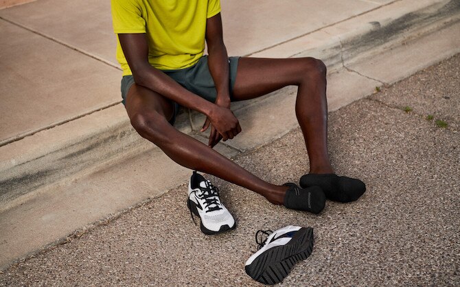 A runner sits on a curb with his shoes off to rest after a tough run.