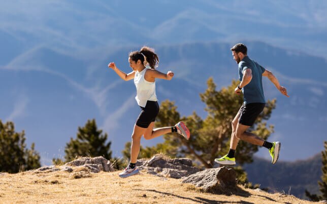 Two people trail running on a sunny hillside