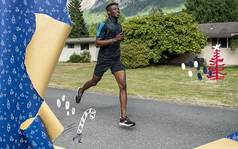 Le coureur souriant en pleine foulée court sur un chemin du quartier avec des maisons et des montagnes en arrière-plan.