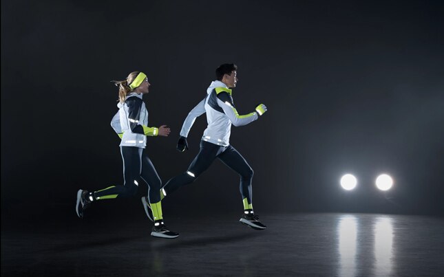 Side view of a runner running on a road at night while wearing reflective gear.