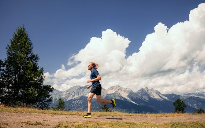 A runner jogs on a dirt trail on a sunny day.