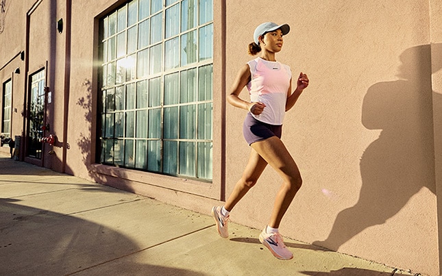 Woman running on the sidewalk in the city in shorts, a workout tank, a hat, and the Ghost 18
