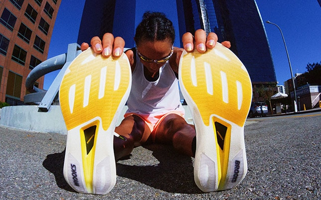 Runner stretching on a city street, with shoe soles facing the camera.