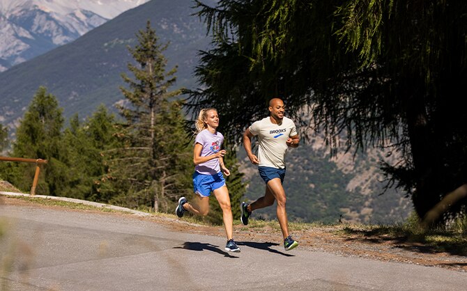 Zwei Läufer*innen auf leerer Straße, umgeben von Bergen und Bäumen