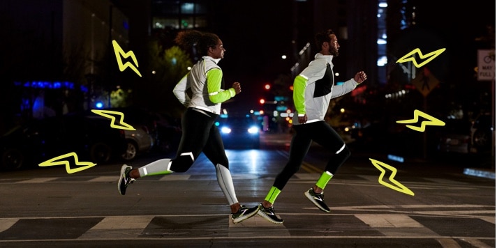Side view of two runners running on a road at night while wearing reflective gear