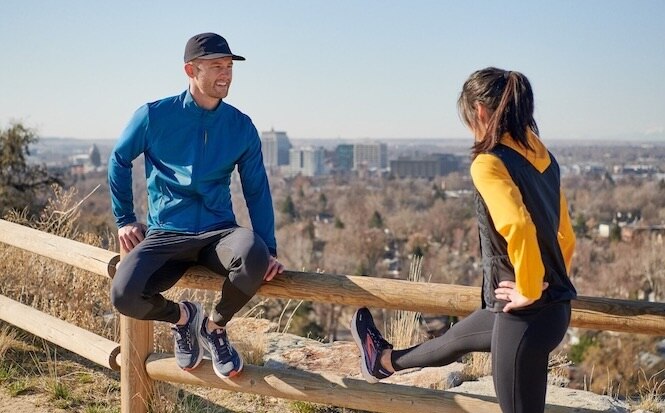 Two runners chat and stretch their hamstrings before a run.