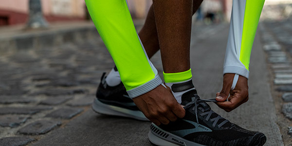 A closeup shot of a runner wearing Brooks Nightlife Collection gear and stooping over to tie his shoes. 