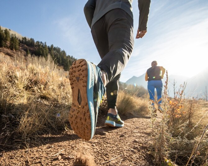 Two runners walking down a trail in the mountains