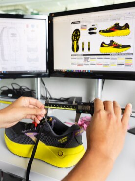 Hands holding trail running shoe in front of computer screen