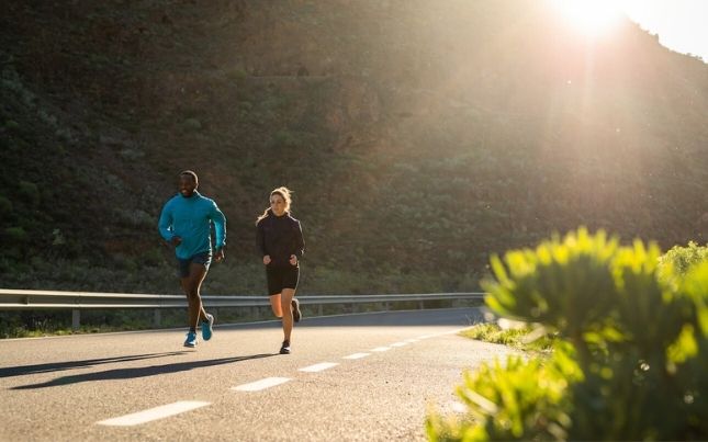 Two runners on a sunny road by a mountain