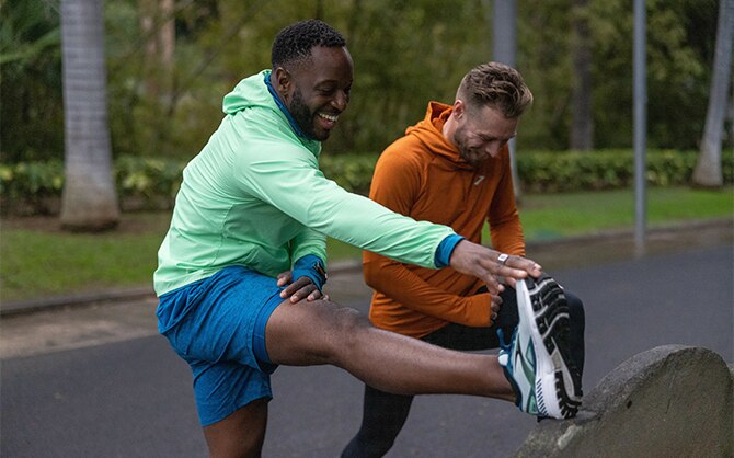 Halbnahaufnahme von zwei Läufern in Brooks Ausrüstung, die Dehnübungen machen