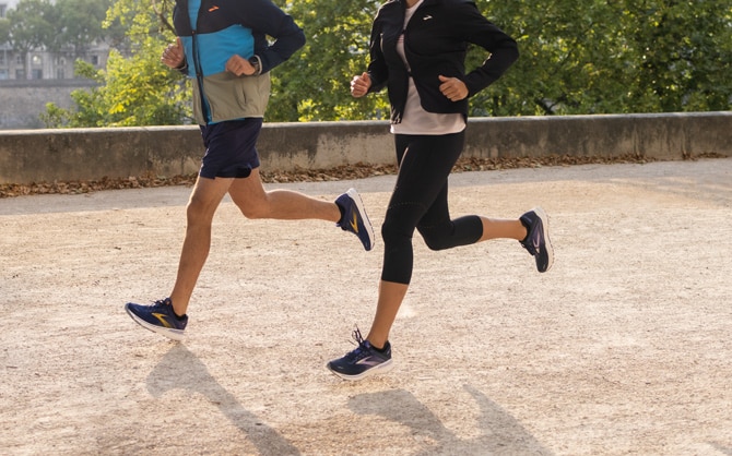 Deux runners, un homme et une femme, dans un environnement type parc urbain.